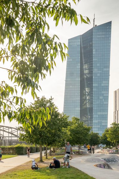 View of the harbour park in Frankfurt with skate park, trees and the European Central Bank in the background, in sunny weather and lively activity.