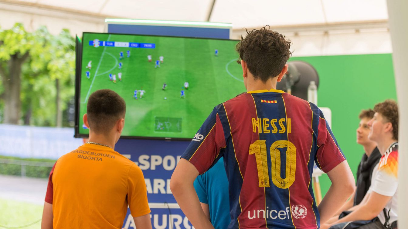 Zwei Jungen spielen ein Fußball-Videospiel in der E-Sport-Area der Fan Zone Mainufer während der UEFA EURO 2024 in Frankfurt. Einer trägt ein Messi-Trikot.