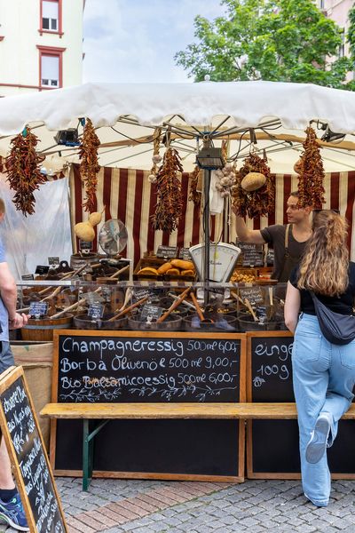 Market stall with vinegar, spices and bread, customers stand in front of the vendor.