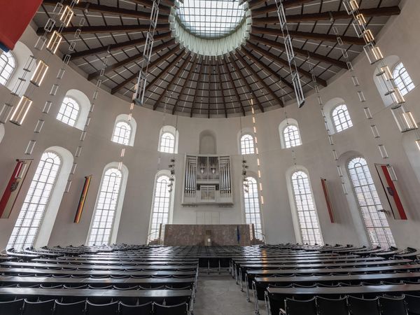 Innenraum der Frankfurter Paulskirche mit runder Kuppeldecke, großen Fenstern und einer Orgel an der Stirnwand. Zahlreiche Sitzreihen und moderne Hängelampen ergänzen das helle, symmetrische Design der historischen Versammlungshalle.