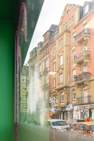 Reflection of colourful old building facades in the window of a modern shop in the Brückenviertel, with cars and urban flair in the street scene.