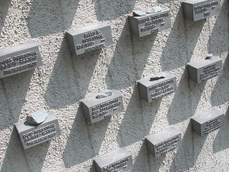 A wall with plaques bearing the names of deported and murdered Jewish people, each with memorial stones.