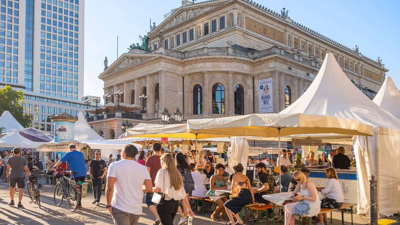 Menschen flanieren und sitzen beim Opernplatzfest vor der Alten Oper in Frankfurt. Die Stände und Sonnenschirme laden zum Verweilen ein.