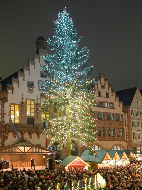 Beleuchteter Weihnachtsbaum auf dem Frankfurter Weihnachtsmarkt 2013 vor der historischen Kulisse des Römers, mit Blick auf die Bühne und auf geschmückte Marktstände. Im Vordergrund sind viele Menschen zu sehen. Das Bild zeigt eine festliche Atmosphäre am Abend.