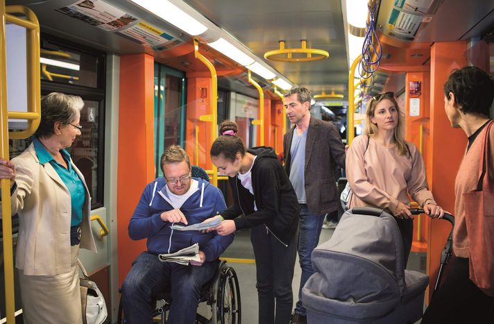 Eine ältere Dame, ein Rollstuhlfahrer und zwei Damen mit Kinderwagen fahren in einer U-Bahn.