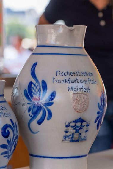 Große traditionelle Bembel mit der Aufschrift „Fischerstechen Frankfurt am Main“, präsentiert auf einem Stand.