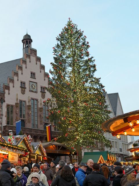 Beleuchteter Weihnachtsbaum auf dem Frankfurter Weihnachtsmarkt 2012 vor der historischen Kulisse des Römers, mit geschmückten Marktständen im Vordergrund und vielen Menschen. Das Bild zeigt eine festliche Atmosphäre am Tag.