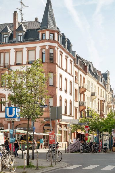 Street scene on Leipziger Straße in Frankfurt with old buildings, an underground sign, bicycles and hustle and bustle under a clear sky.