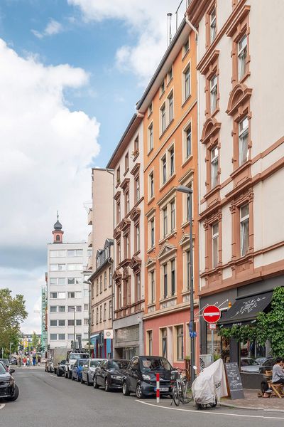 A street scene in Frankfurt's Brückenviertel with historic buildings, shops and street cafés. Bicycles and cars characterise the lively street scene under a clear sky.