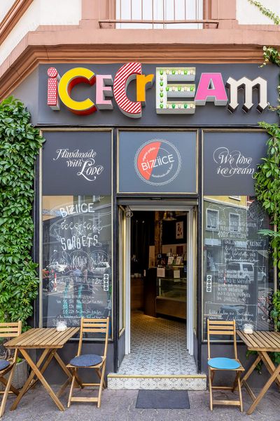 Ice cream shop with colourful ‘Ice Cream’ sign and cosy outdoor seating area, surrounded by climbing plants on the façade, in Frankfurt's Brückenviertel district.