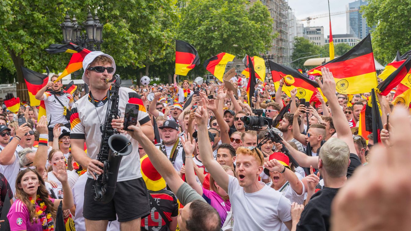 Ein Mann spielt umgeben von einer Menge Deutschland-Fans in Fußballtrikots Saxophon. 