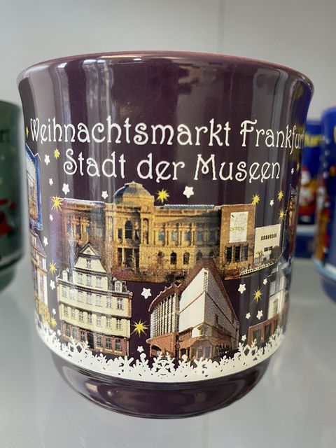 Lilafarbene Glühweintasse mit den Frankfurter Museen wie dem Städel, dem Goethe-Haus und dem Museum für Moderne Kunst. Über den Abbildungen steht Weihnachtsmarkt Frankfurt Stadt der Museen. 